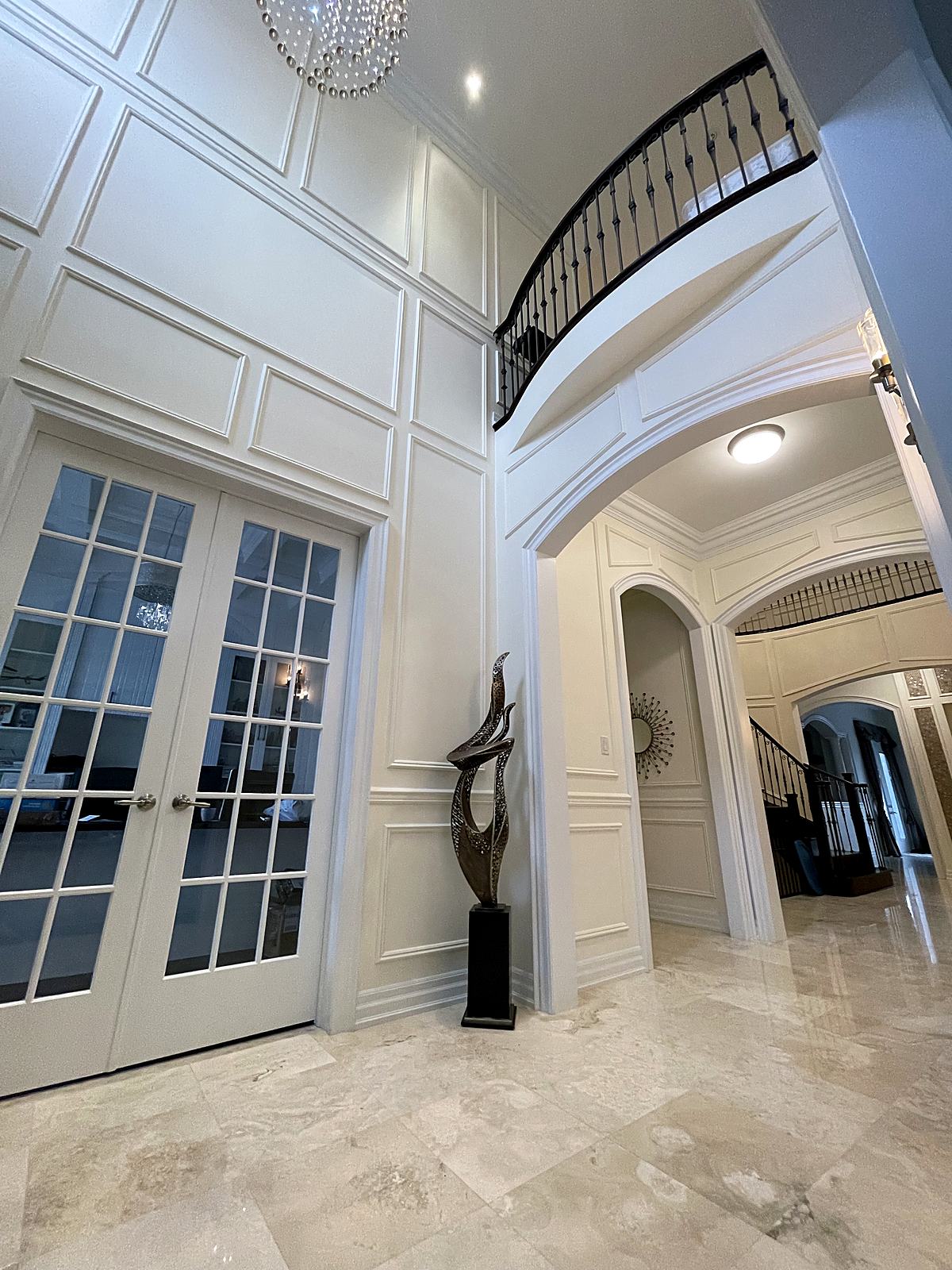 Two-storey foyer with white wall panelling, arches and iron railing