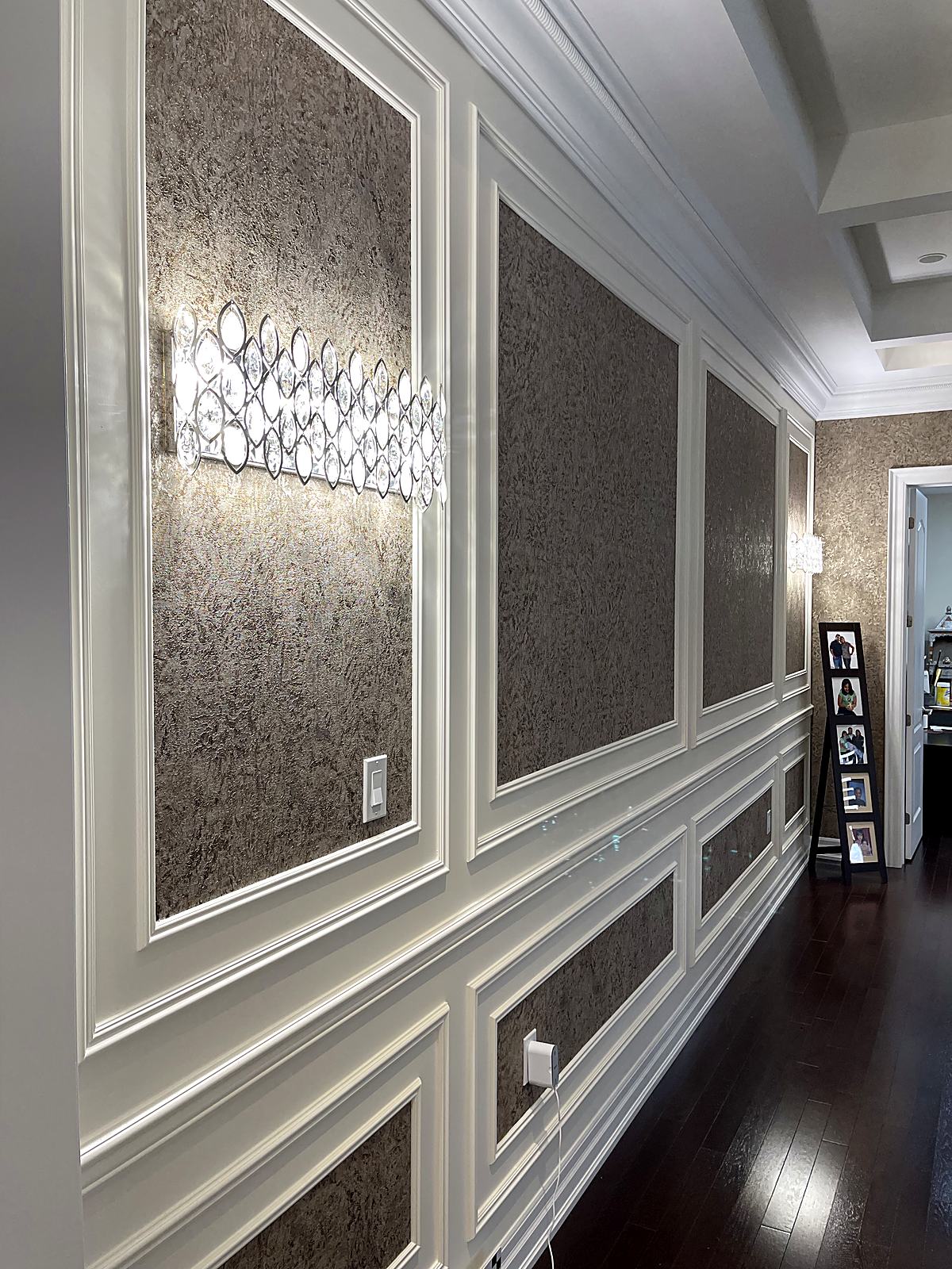 Hallway wainscoting with metallic wallpaper panels and a crystal wall sconce